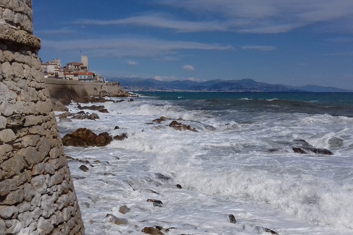 The sea ramparts of old Antibes, waves breaking on the rocks with the old town beyond
