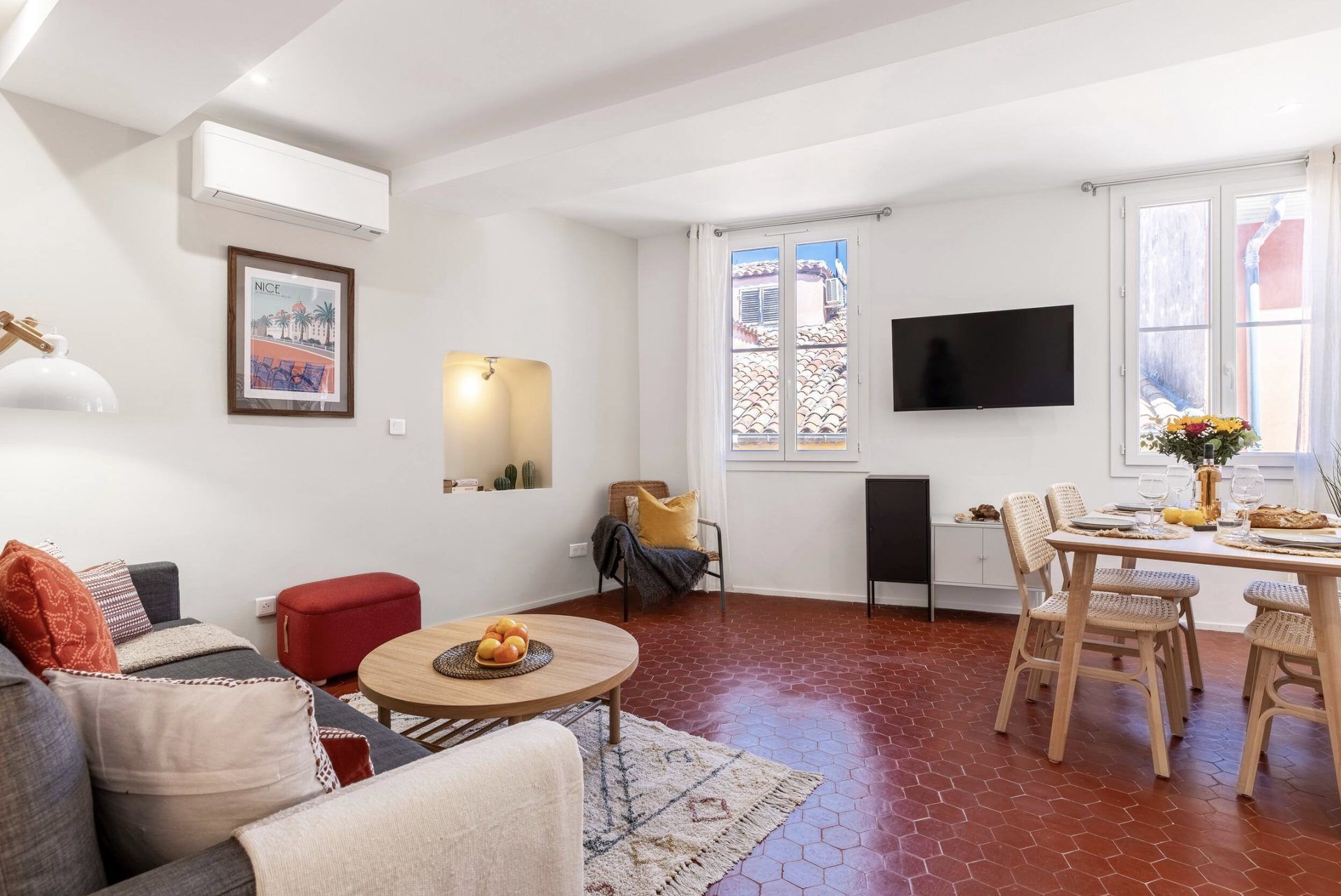 Open-plan living and dining room at Gilli — sofa, wall-mounted TV, dining table, and two windows onto the Old Town