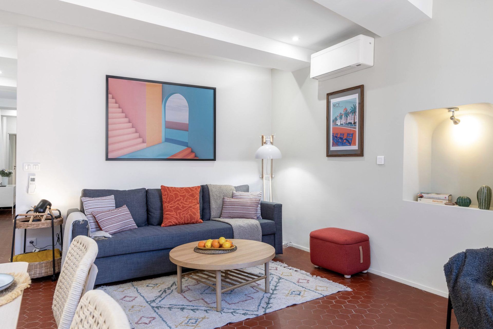 Living corner at Gilli with a blue sofa, red pouf, terracotta tomette floor, and colourful artwork